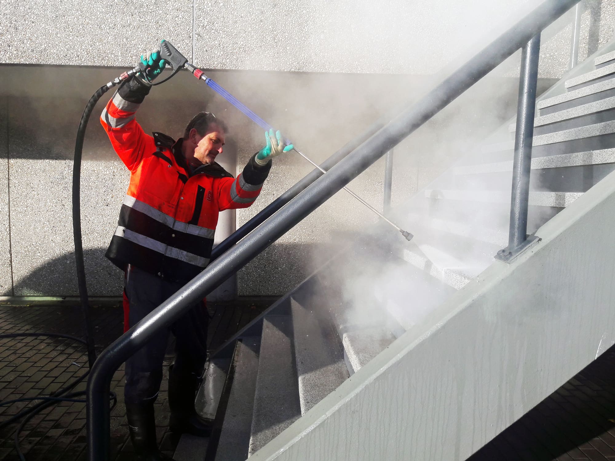 On the stairs of the RAI Conference Center in Amsterdam a man cleans its stone steps from dirt and graffiti using a hot pressure washer.